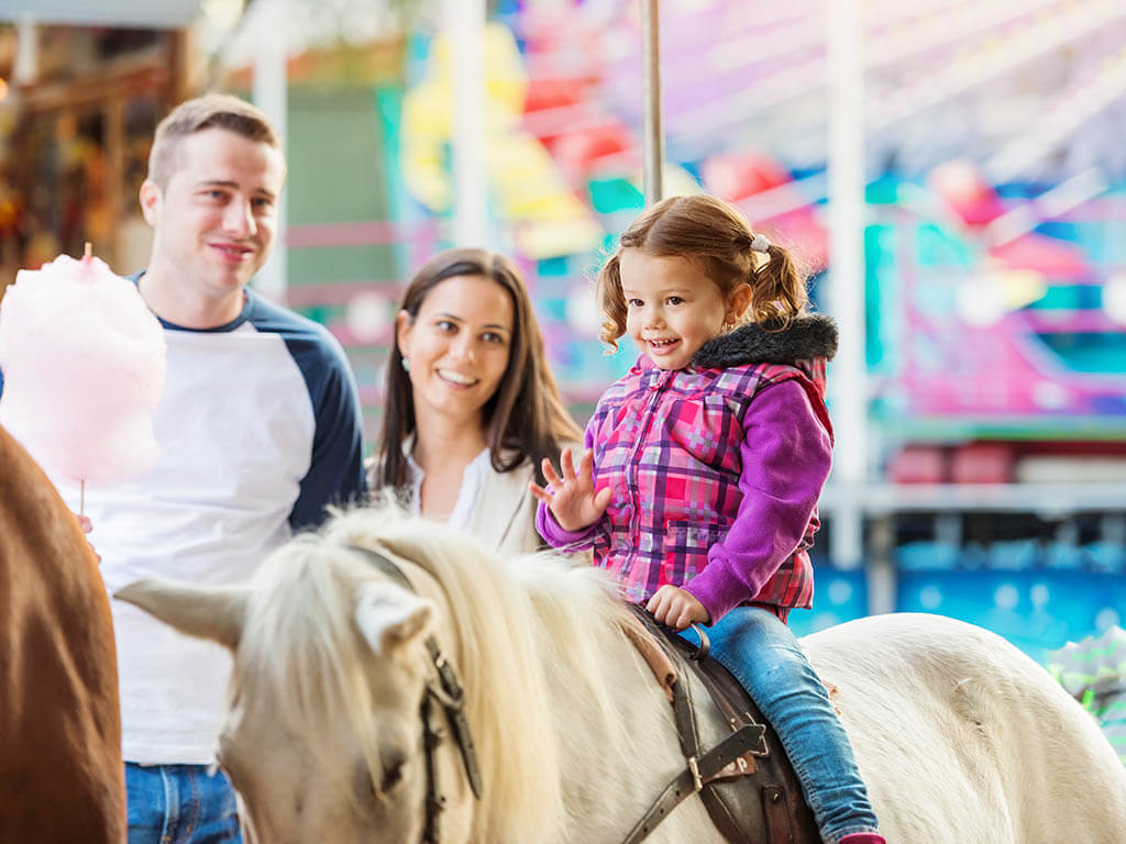 Kleines Mädchen mit Eltern beim Ponyreiten auf Volksfest